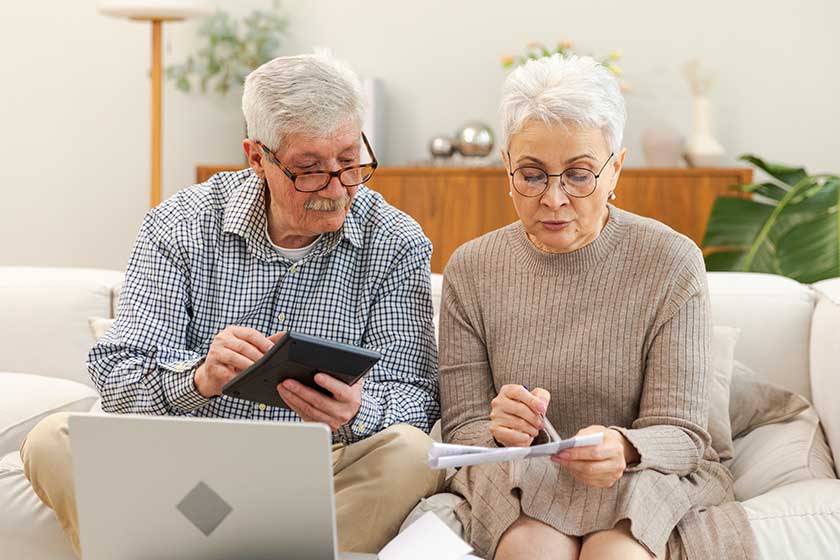 Middle aged senior couple sit with laptop and paper document. Older mature man woman reading paper bill pay online at home managing bank finances calculating taxes planning loan debt pension payment