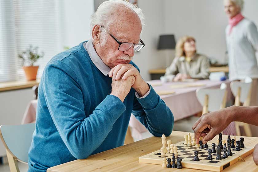 Pensive senior man in eyeglasses concentrating on his play in chess, he playing with his friend at table Pensive senior man in eyeglasses concentrating on his play in chess, he playing with his friend at table