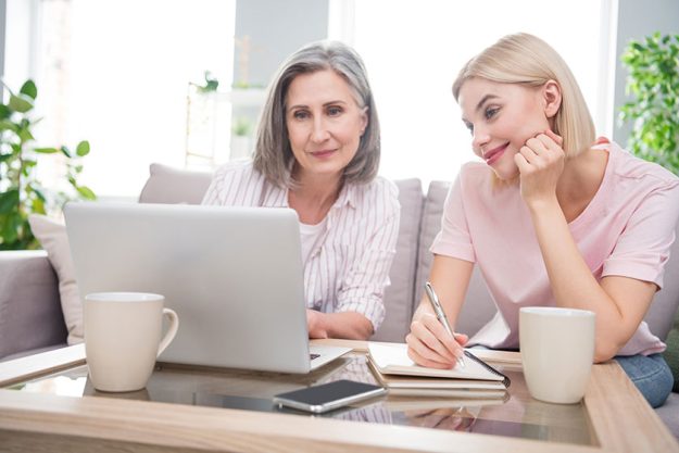 Photo of happy charming grey haired retired woman blonde lady sit sofa look laptop write note in house indoors
