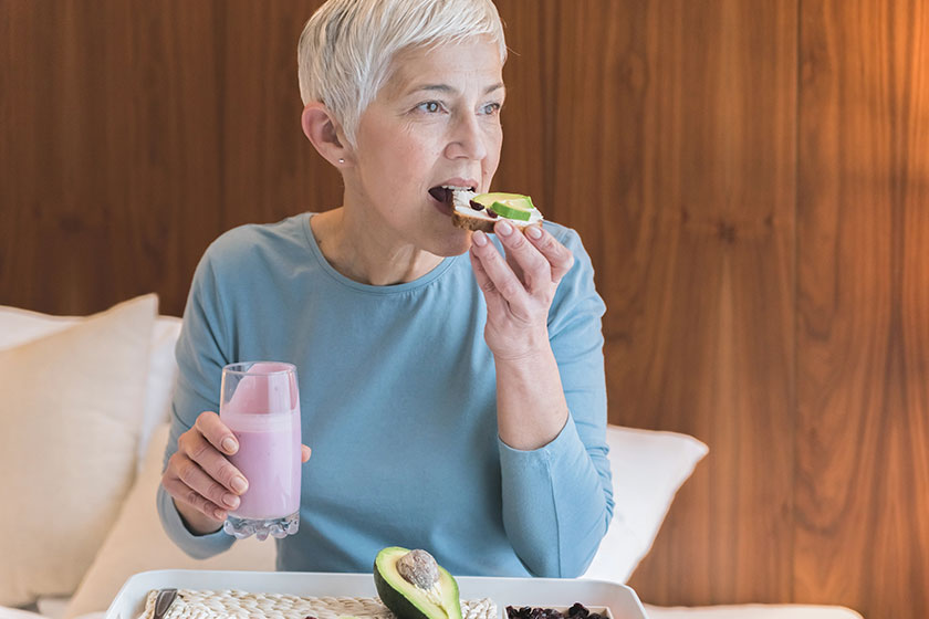 Portrait of beautiful senior woman drinking pink fruit smoothie and eating healthy toast with avocado Portrait of beautiful senior woman drinking pink fruit smoothie and eating healthy toast with avocado
