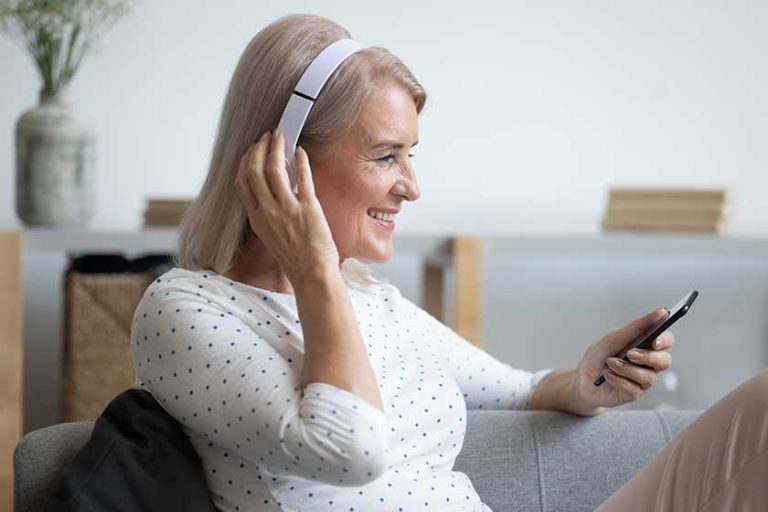 Smiling mature woman in headphones enjoying music, using phone