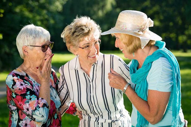 Three elderly female friends gossiping outdoors while standing in park