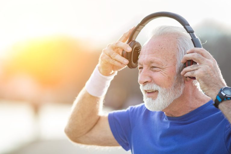 Senior smiling man with beard in sportswear puts on headphones and prepares for exercise in nature — Photo