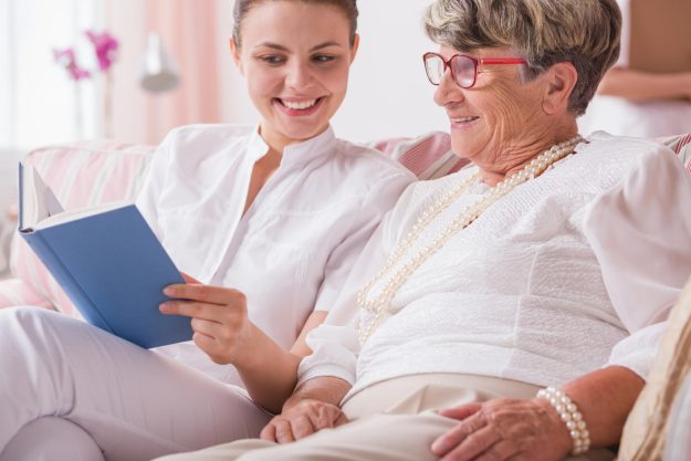 Smiled,Nurse,And,Senior,Woman,Sitting,Together,On,A,Couch