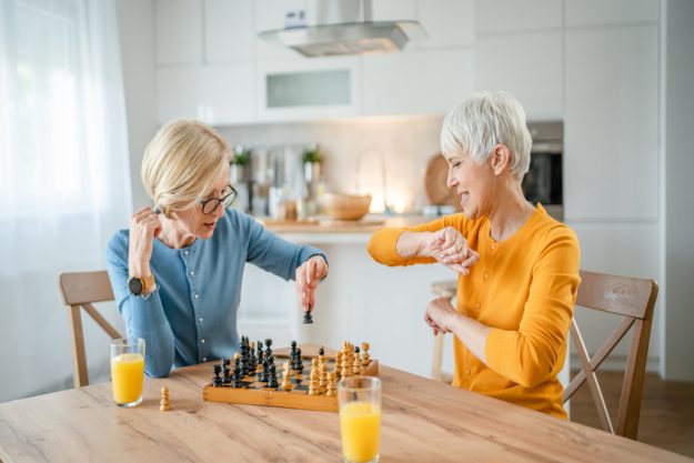 two women mature senior females sisters play chess board game at Two senior mature women caucasian female woman friends or sisters play leisure chess board game at home— Photo