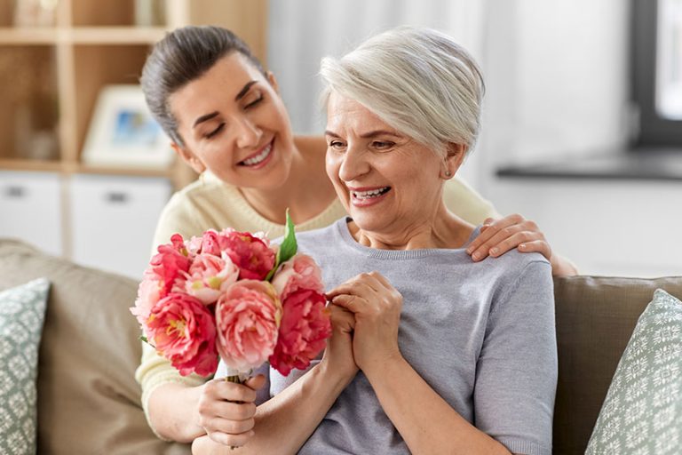 Adult-daughter-giving-flowers-to-old-mother