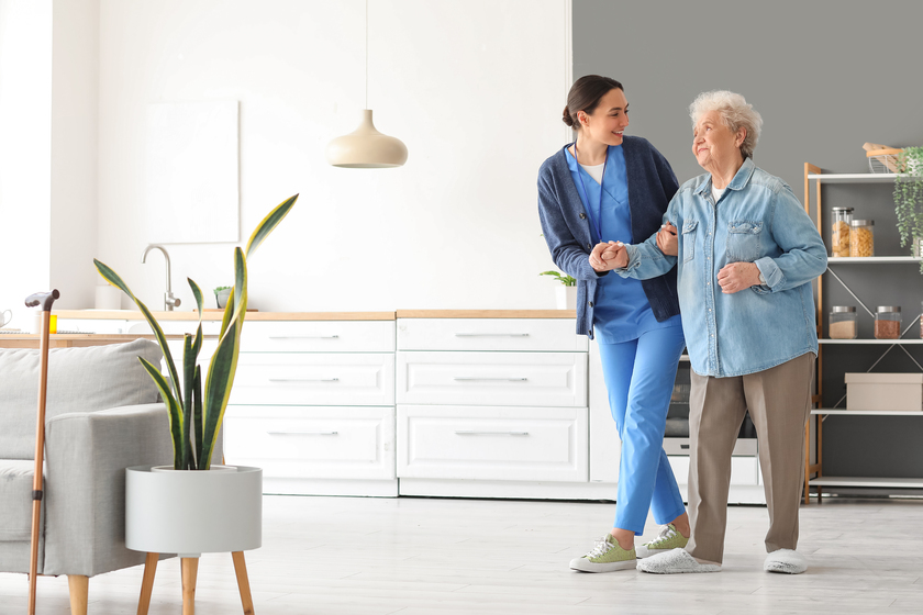 Young caregiver helping senior woman to walk in kitchen — Photo