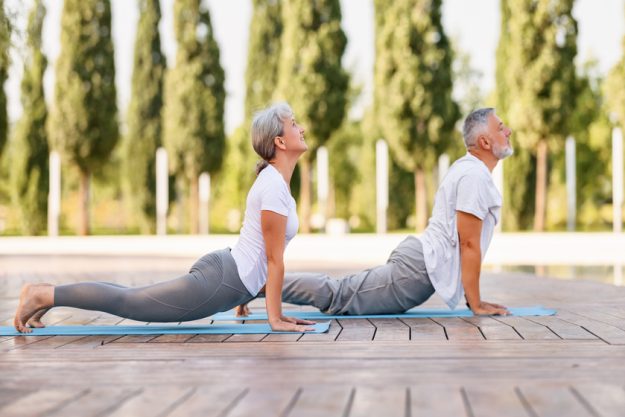 Active mature family man and woman doing yoga exercise stretch their back, taking the cobra pose while exercising in morning on fresh air, senior couple practicing Bhujangasana — Photo