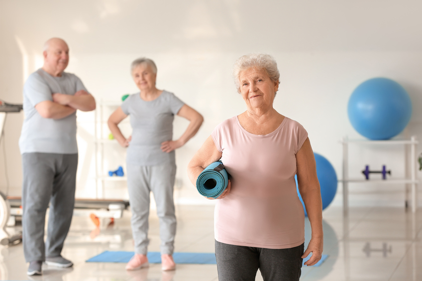 Elderly woman with yoga mat in gym — Photo