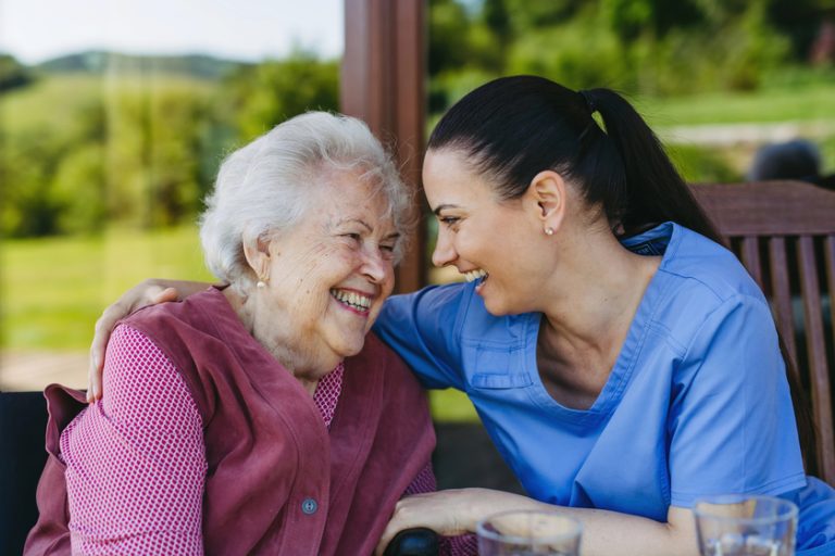 Portrait of female caregiver and senior woman embracing. Nurse and elderly woman enjoying a warm day in nursing home, public park. — Photo