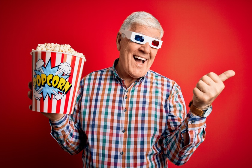 Senior hoary man watching film using 3d glasses eating popcorn over red background pointing and showing with thumb up to the side with happy face smiling — Photo