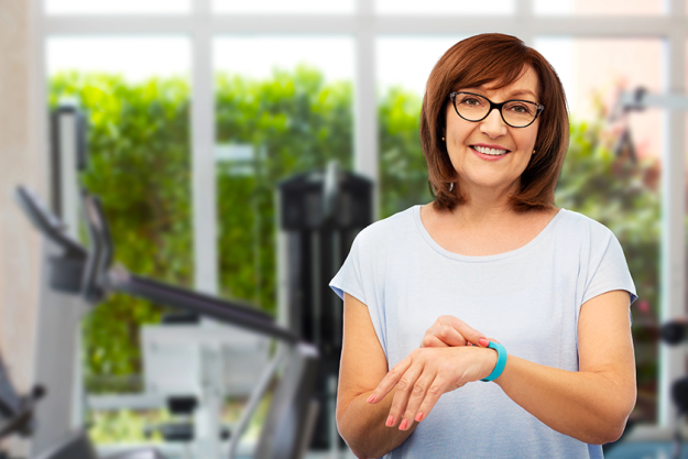 Smiling senior woman with fitness tracker over gym