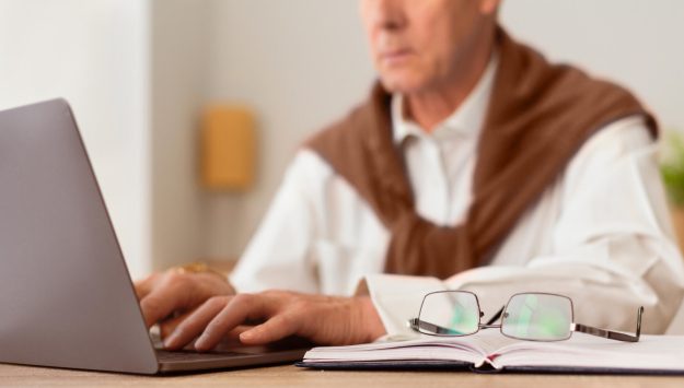 Unrecognizable Senior Businessman Working On Laptop Sitting In Office, Cropped