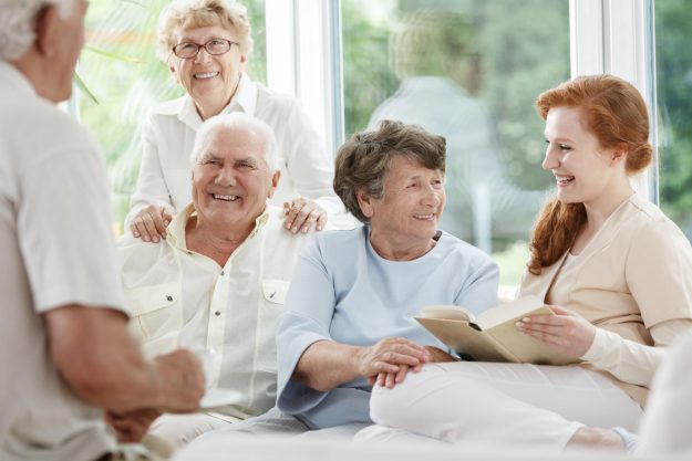 Smiling,Nurse,Holds,Book,And,Sitting,Next,To,Happy,Elder