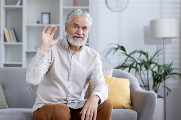 Senior man on a video call waving at the camera from home